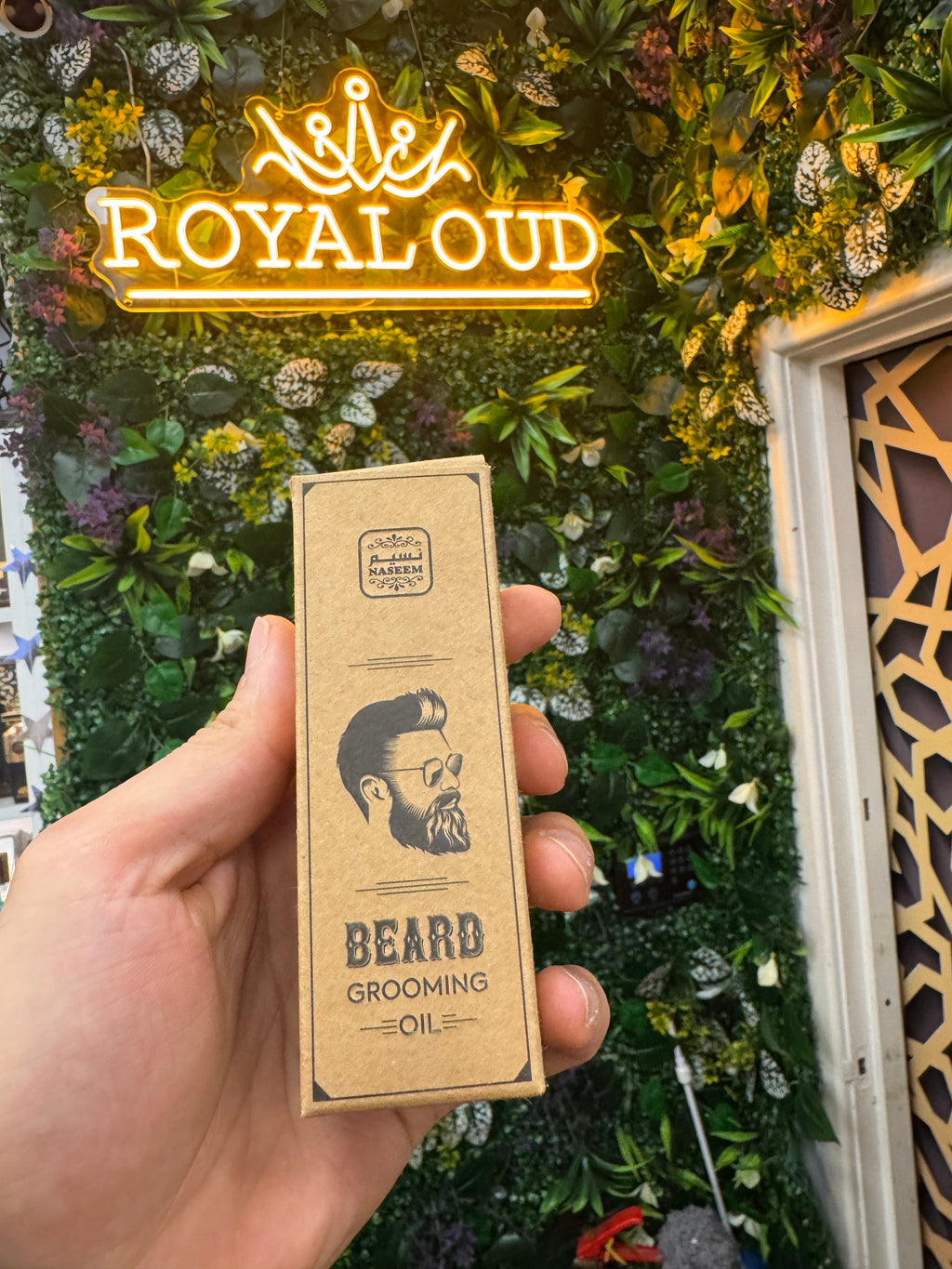 Hand holding a box of 'Bear Grooming Oil' with 'Royaloud' branding against a decorative background.