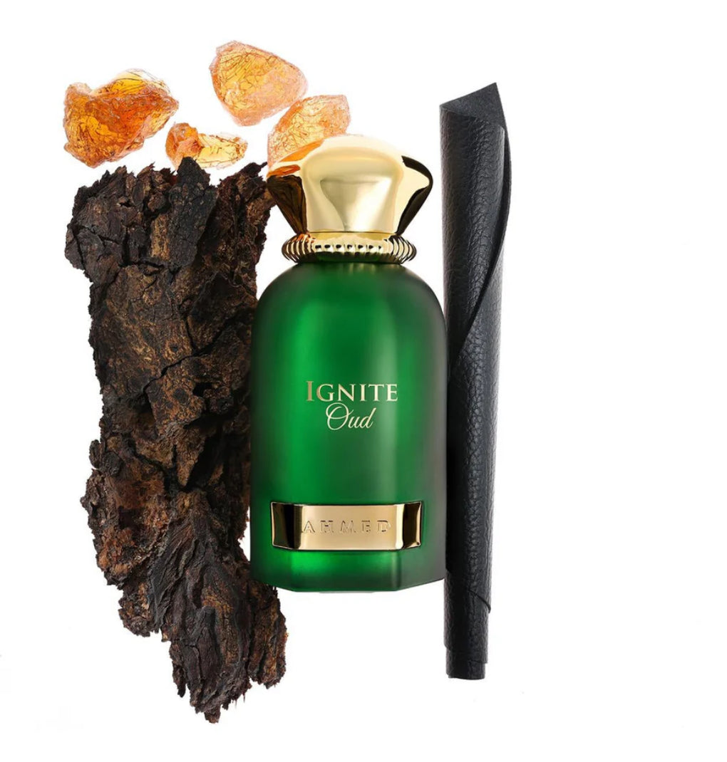 Green perfume bottle labeled 'Ignite Oud' with gold cap and base, surrounded by amber stones and dark wood on a white background.