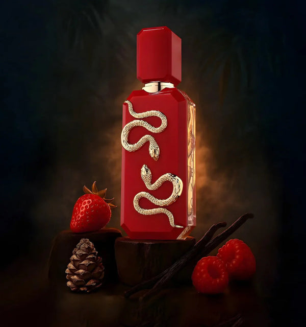 Red perfume bottle with gold accents on a dark background with berries and a pine cone.