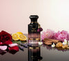 Perfume bottle labeled 'Oud & Roses' surrounded by flowers and fruits on a reflective surface.