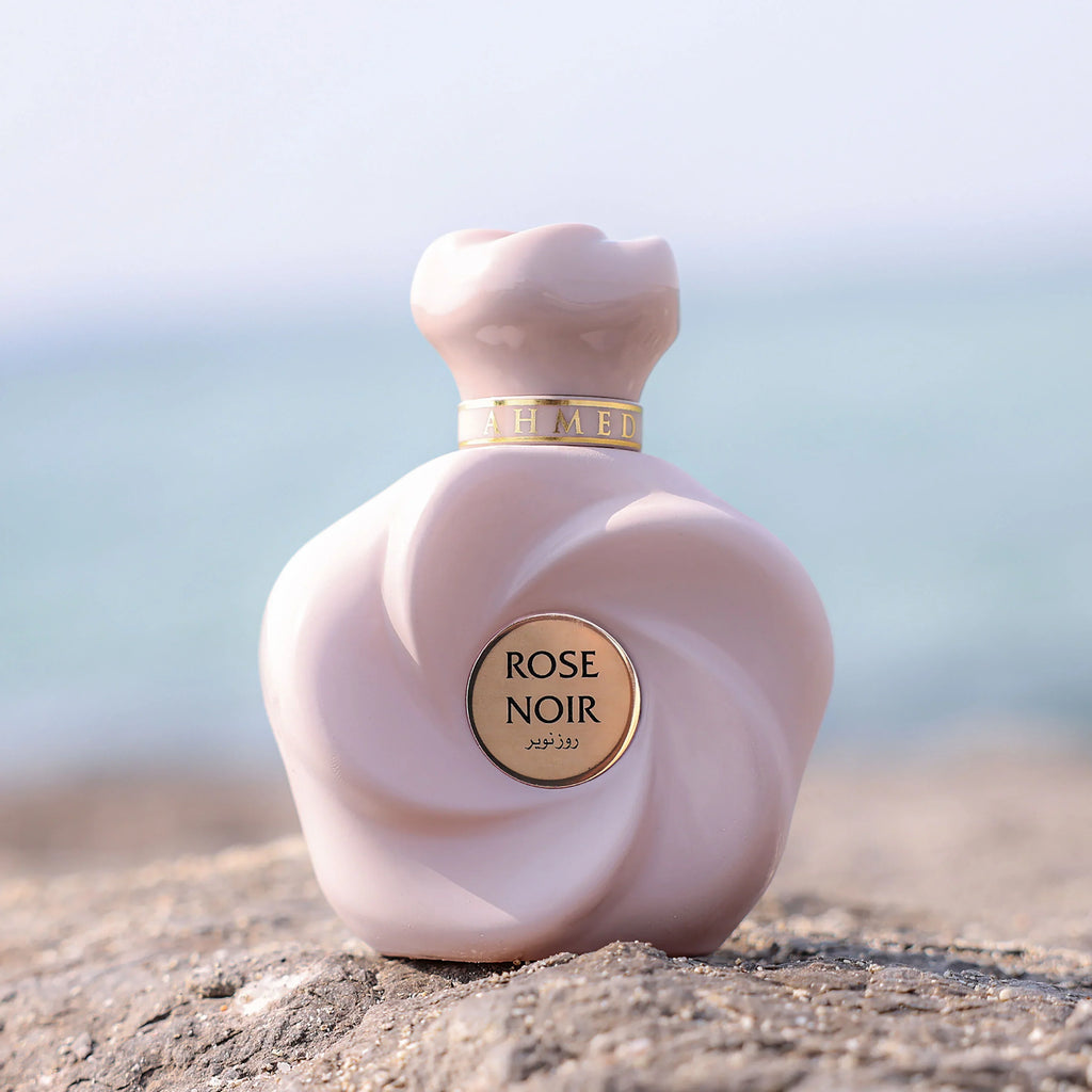 Pink 'Rose Noir' perfume bottle on a rock with a blurred natural background
