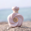 Pink 'Rose Noir' perfume bottle on a rock with a blurred natural background